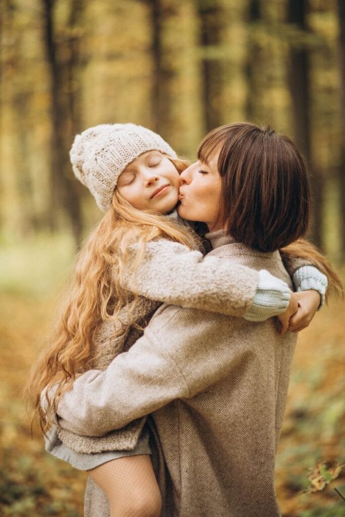 Mãe abraçando e beijando a filha no colo em um parque, representando a evolução da menina à mulher na Noutrina.