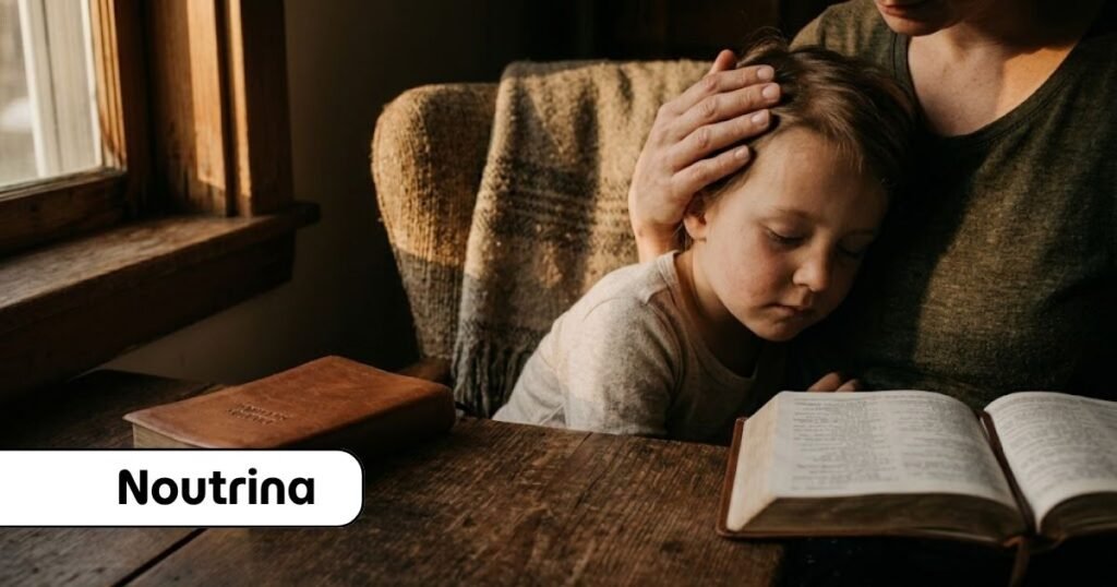 Mãe acolhe o filho pequeno que repousa a cabeça em seu peito, enquanto mantém a mão sob a cabeça dele, sentados à mesa de madeira rústica com uma Bíblia aberta sob a luz suave da janela, representando a constância na educação cristã dos filhos.