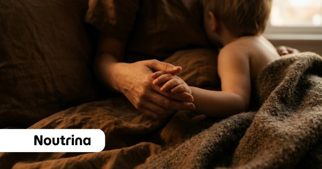 Uma mãe segura delicadamente a mão pequena de seu filho deitado na cama sob um cobertor texturizado em tons terrosos escuros, transmitindo afeto e conexão íntima sobre como ensinar o filho sobre Deus. No canto inferior esquerdo, há um selo branco com o logotipo "Noutrina" escrito em letras pretas.